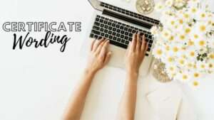 Certificate wording concept with hands typing on a laptop on a clean white desk decorated with flowers.