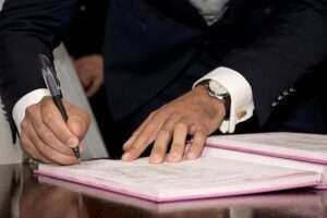 Close-up of a person in a dark suit signing a document or guestbook with a pen
